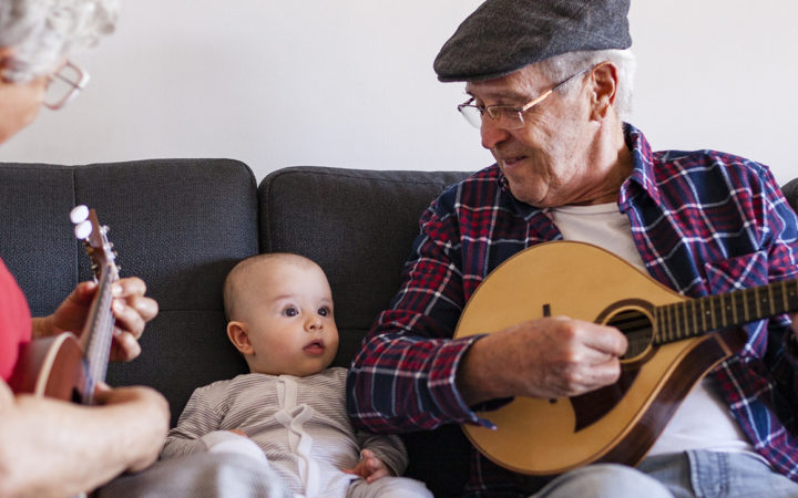Vanhempi mies ja nainen soittavat vauvalle kitaraa.