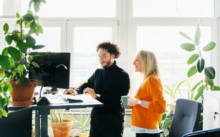 Two Colleagues Looking At Work Using Standing Desk