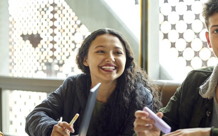 Hymyilevä nainen keskustelee ystäviensä kanssa pöydän äärellä.