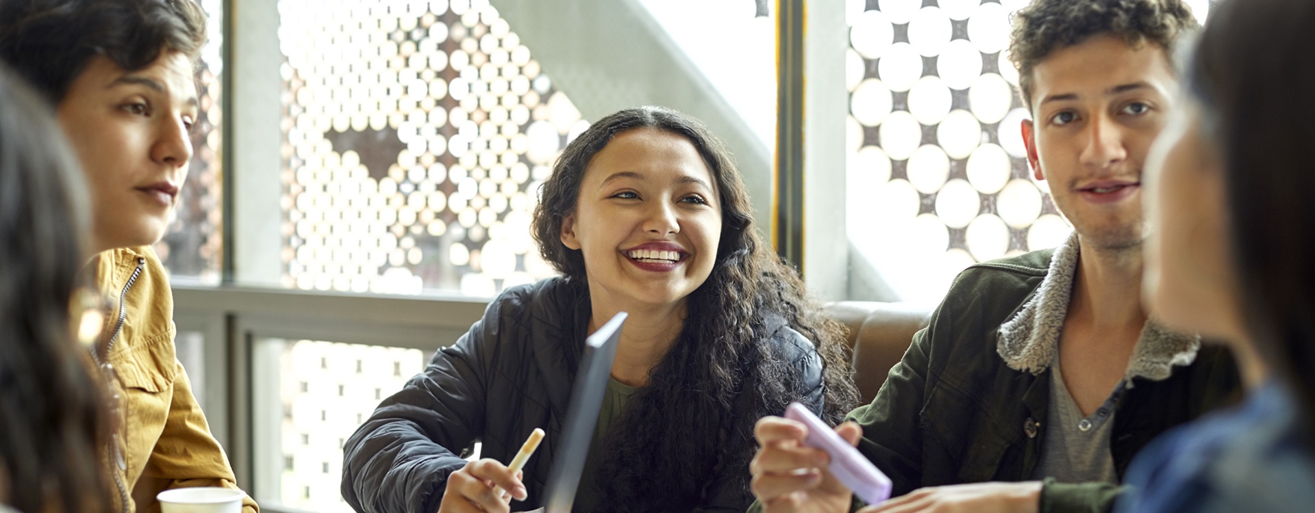 Hymyilevä nainen keskustelee ystäviensä kanssa pöydän äärellä.