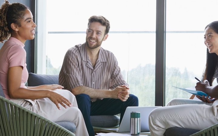 Neljä työkollegaa istumassa nojatuoleissa ja keskustelemassa. Yksi tekee muistiinpanoja.