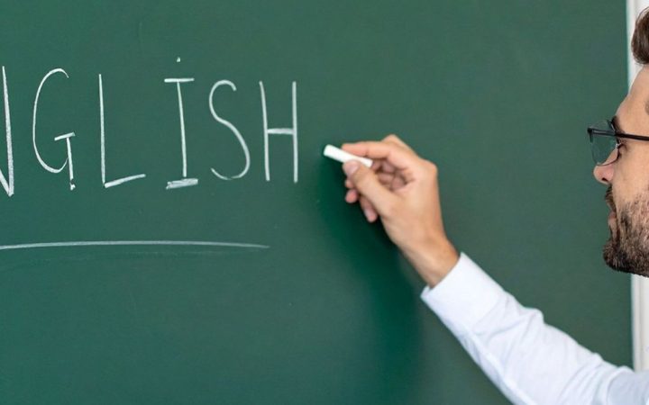 Mies kirjoittaa liitutaululle sanaa English.