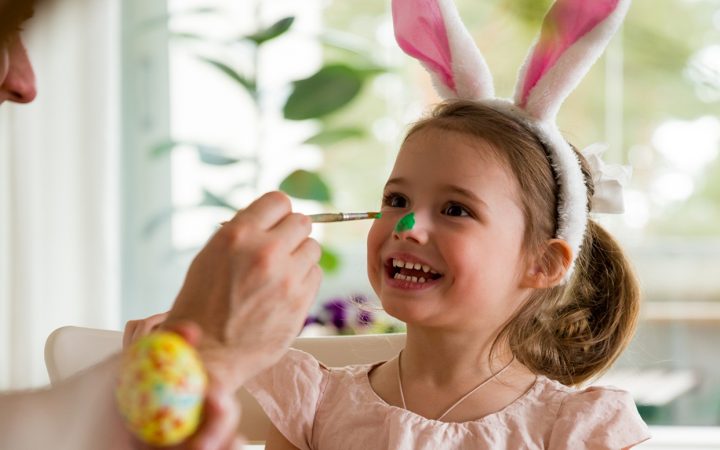 Isä ja tytär maalaamassa pääsiäismunia, ja tytön nenää vihreäksi. Tytöllä on päässään pupunkorvat,