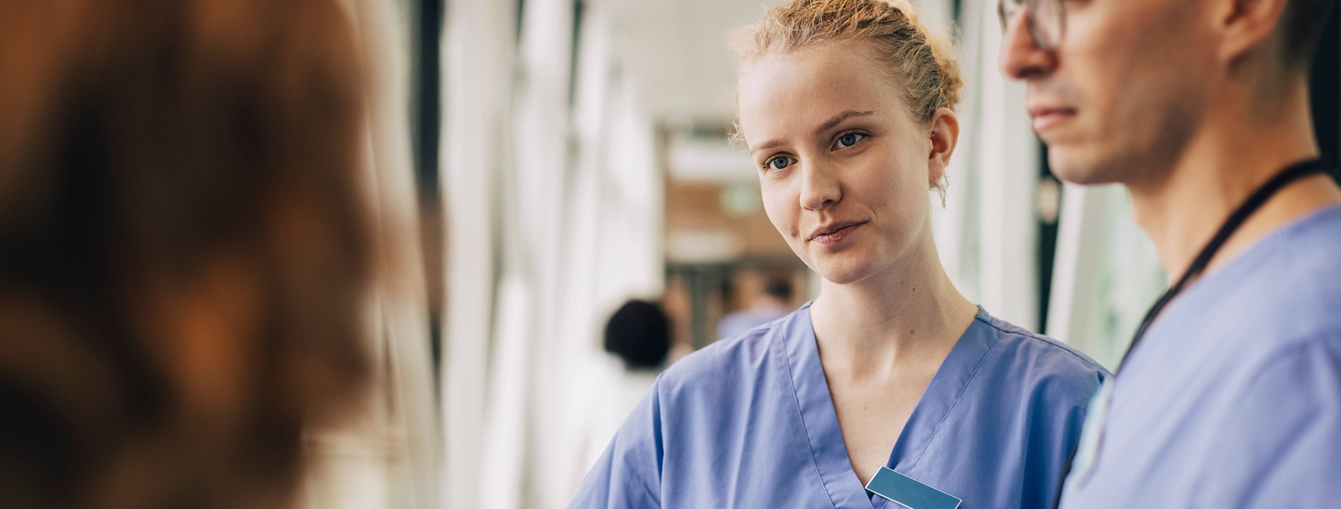 Nuori naishoitaja kuuntelee asiakasta kollegan seisoessa vieressä.