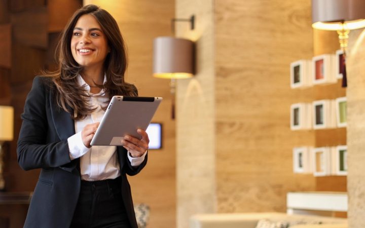 Nuori liikenainen pitää tablettia kädessään ja kävelee yrityksensä aulassa.