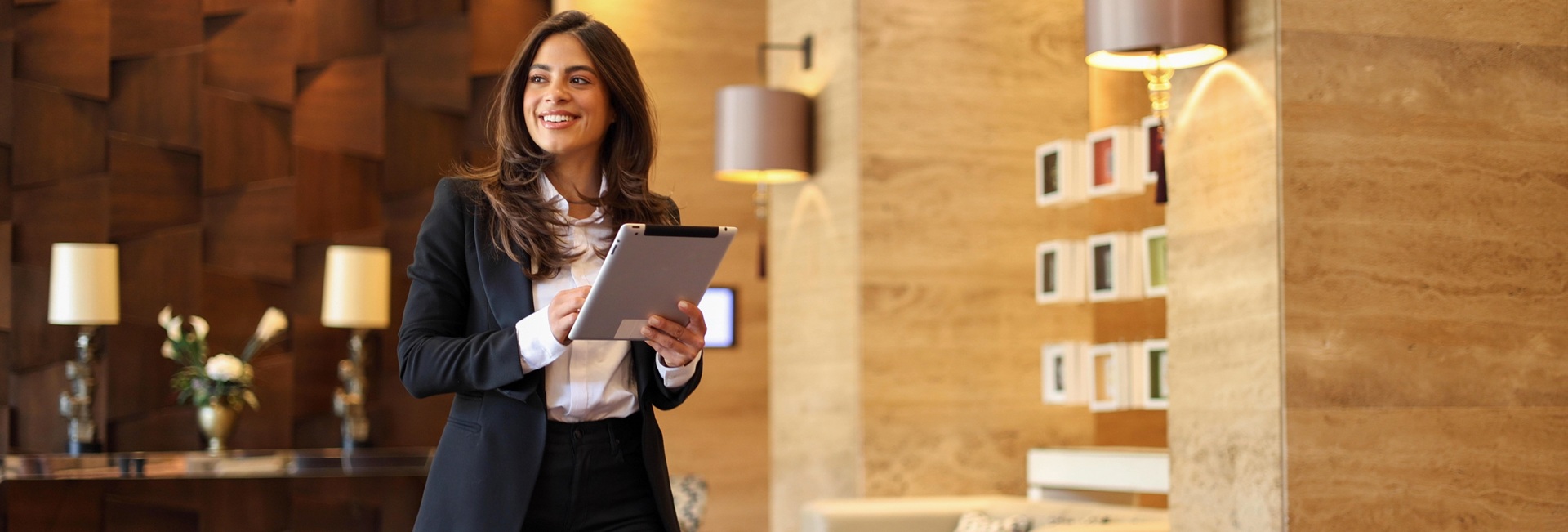 Nuori liikenainen pitää tablettia kädessään ja kävelee yrityksensä aulassa.