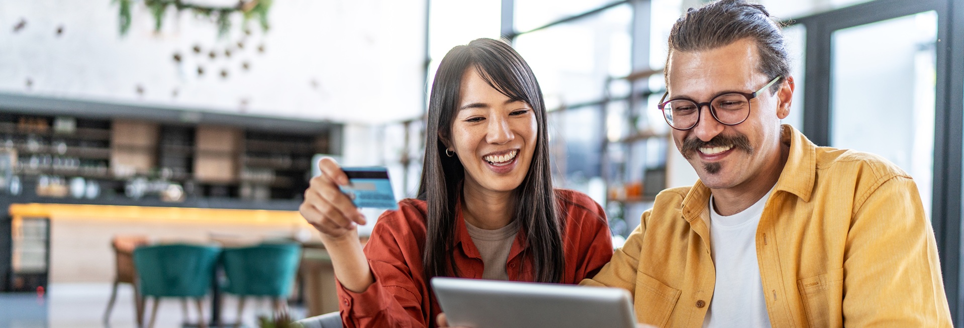 Iloinen pariskunta modernissa kahvilassa, tutkivat jotain tabletilla.