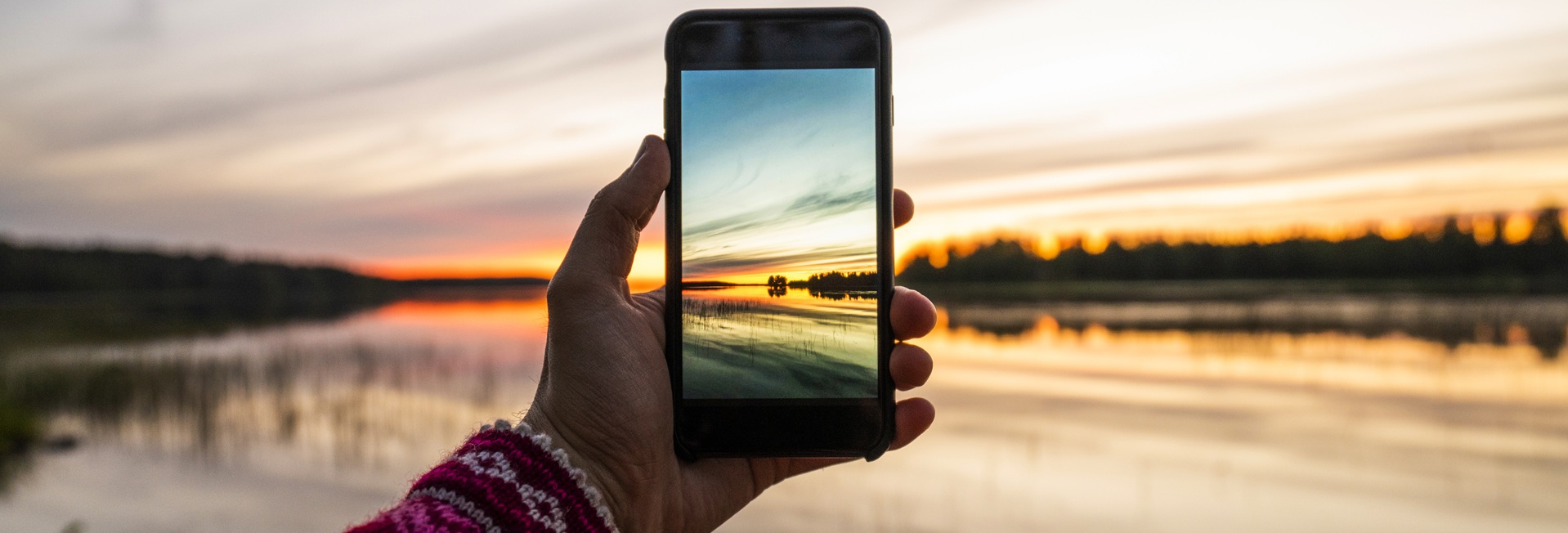 Henkilö ottaa älypuhelimellaan kuvan auringonlaskusta.