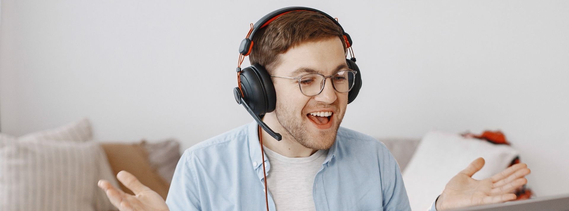 Iloinen mies kuulokkeet päässä opiskelee kannettavalla tietokoneella kotonaan. Vieressä pöydällä myös kirja.