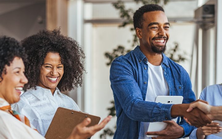 A diverse group of professionals smiling and shaking hands in a modern office environment.
