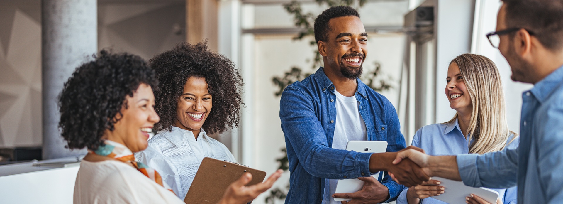 Ryhmä hymyileviä henkilöitä seisomassa ja kättelemässä modernin toimistoympäristön käytävällä.