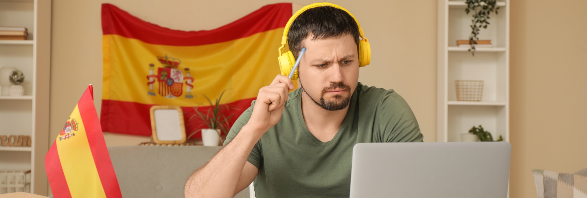 Mies mietteliäänä tietokoneen ääressä opiskelee espanjaa, taustalla Espanjan lippu.