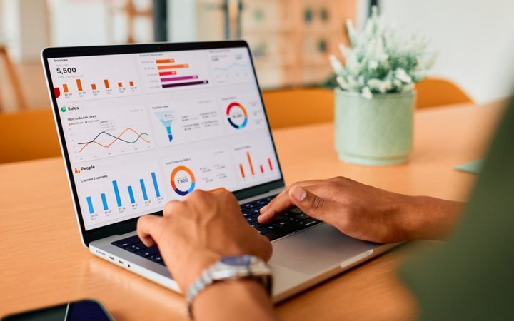 Kannettava tietokone pöydällä. Koneella työskentelevästä henkilöstä näkyy vain kädet.