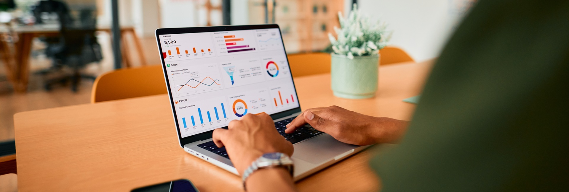 Kannettava tietokone pöydällä. Koneella työskentelevästä henkilöstä näkyy vain kädet.