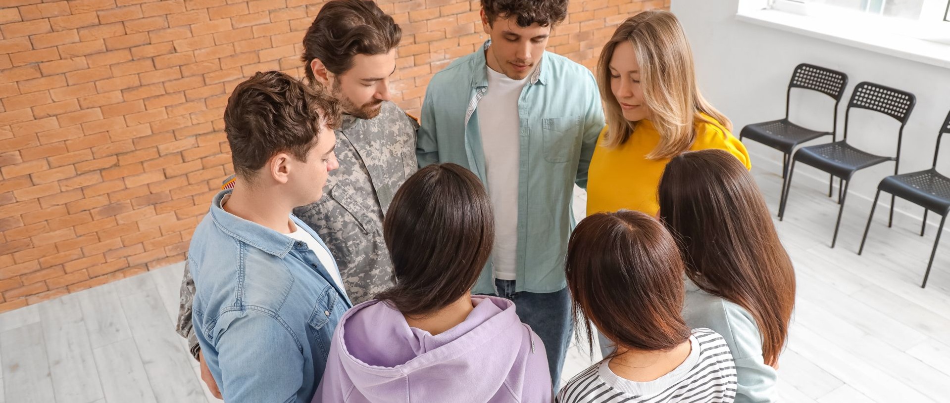 Seitsemän ihmistä seisomassa ringissä silmät kiinni kädet toistensa vyötäröillä.