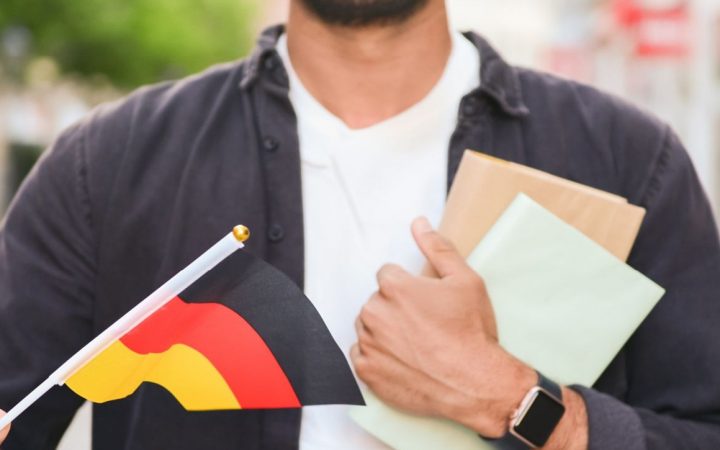 Lähikuva miehestä kirjat ja pieni Saksan lippu kädessä.