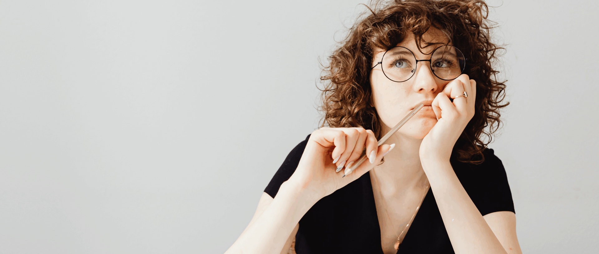 Mietteliäs, silmälasipäinen nainen nojaa toisella kädellään poskeen, toisessa kädessä kynä