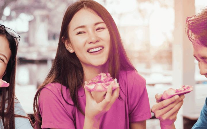 Kolme opiskelijaa istuvat nauraen pöydän ääressä. Jokaisella on kädessään pitsapala.