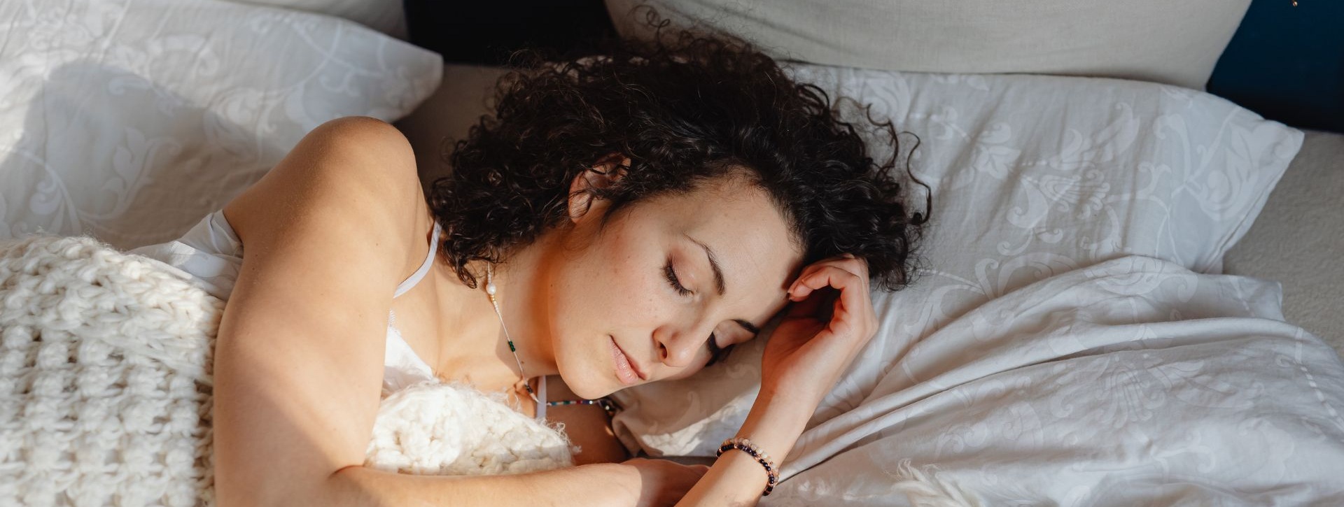 Nainen nukkumassa sängyssä vaalean peiton alla.
